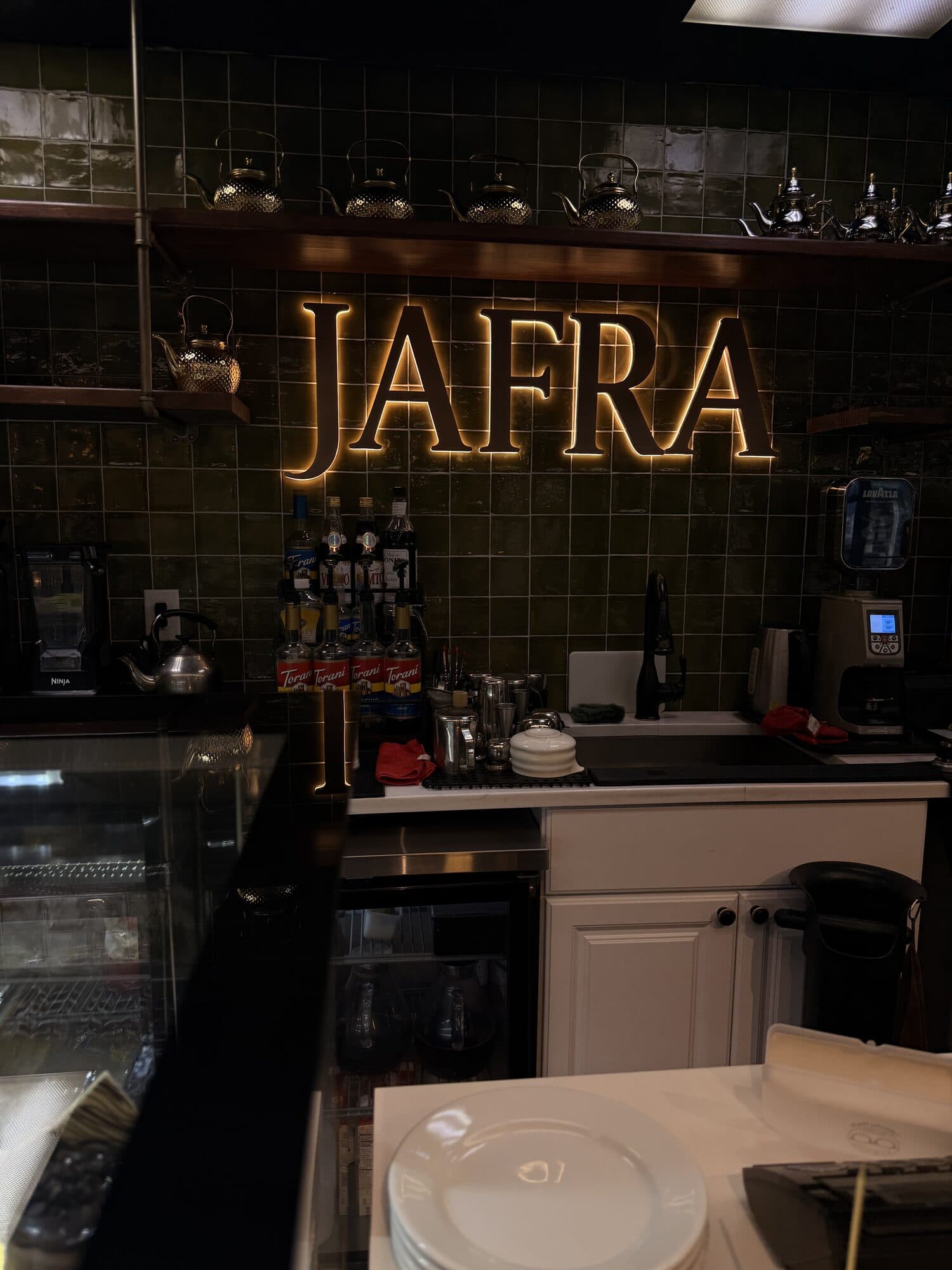 The backlit JAFRA sign above the bar on emerald zellige tile